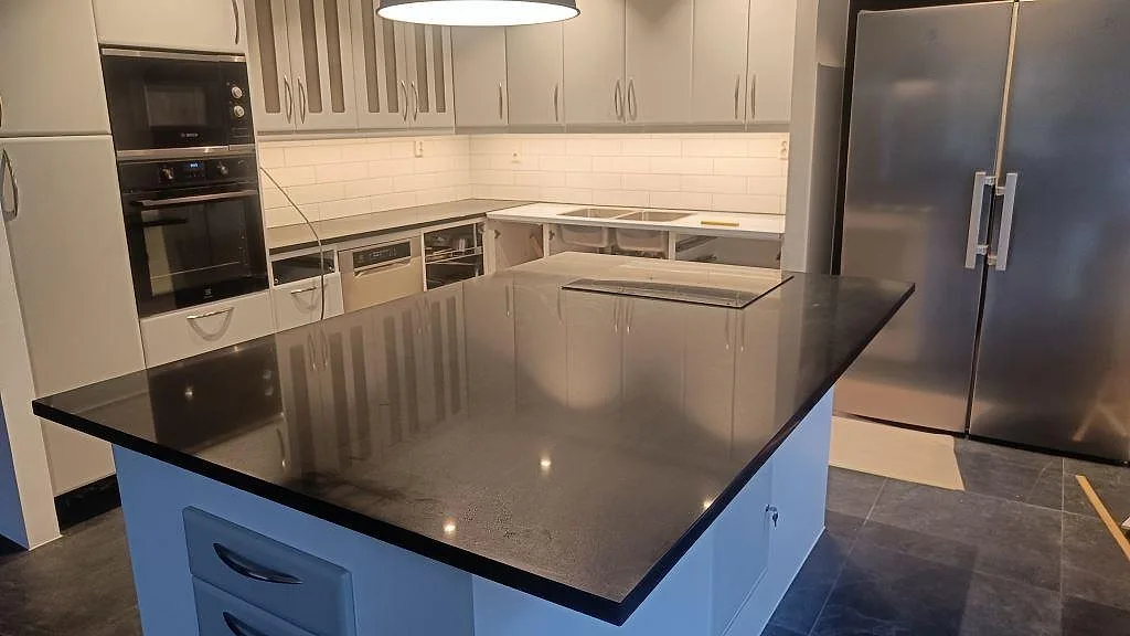 Köksö och köksbänkskiva i polerad Silestone Negro Tebas med mörk yta, blå underskåp och vit kaklad stänkzon i Södra Sandby.