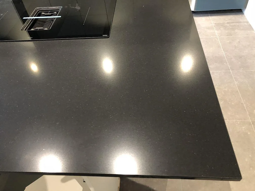 Topp på köksö i svart polerad Silestone Negro Tebas med diskret kvartsglitter och infälld häll, fotograferad uppifrån i ett kök i Svedala.