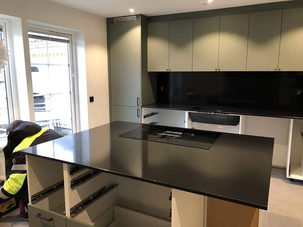 Köksbänkskiva och köksö i svart Silestone Negro Tebas, polerad, med övermonterad induktionshäll i ett kök under montering i Svedala.