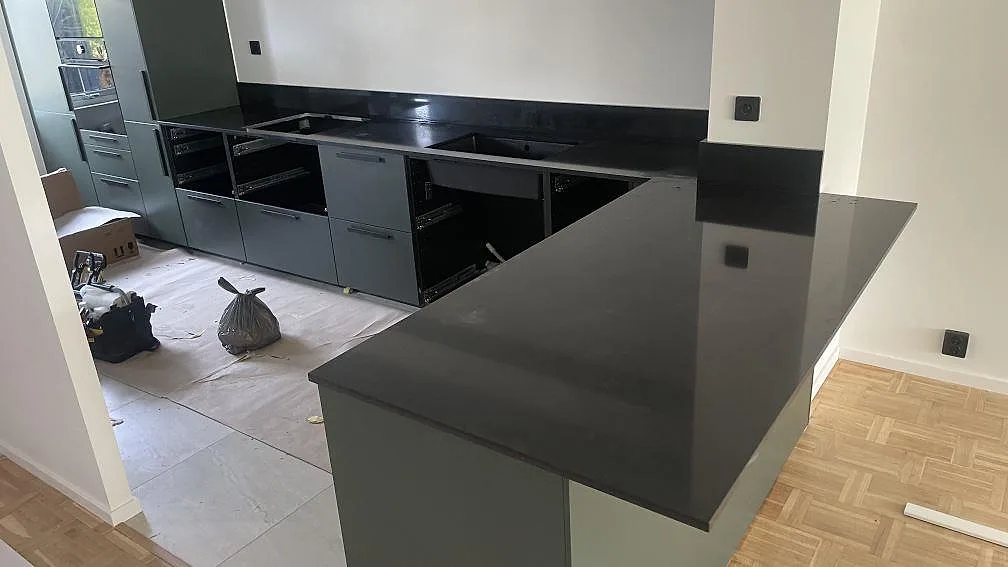 Köksbänkskiva och köksö i svart Silestone Night Tebas, polerad komposit, med uppvikt stänkskydd i ett kök under montering i Oxie.