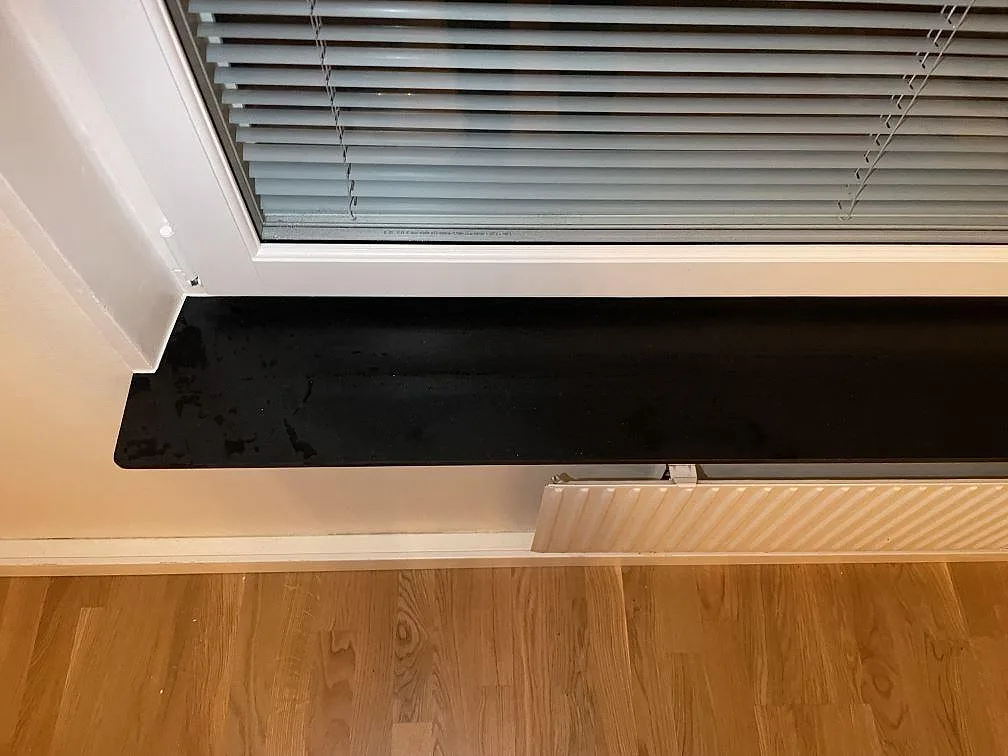 Detalj av Silestone Night Tebas fönsterbänk i matt svart kvartskomposit vid fönstersmyg i Stockholm.