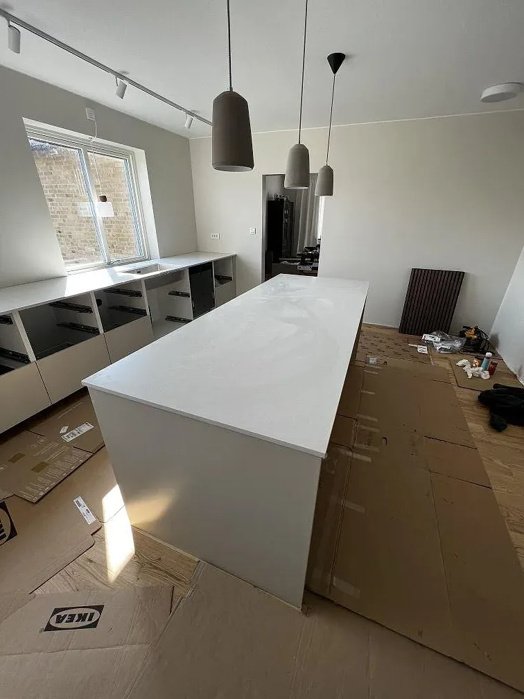 Vit köksö i Silestone Nolita kvartskomposit med pendlar och dagsljus i ett kök i Eslöv.