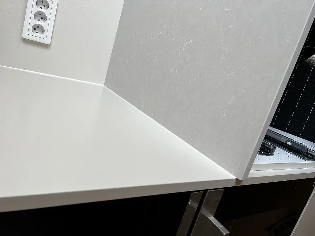 Köksbänkskiva i Silestone Nolita som möter en uppvikt stänkkant i samma greige sten i ett kök i Eslöv.
