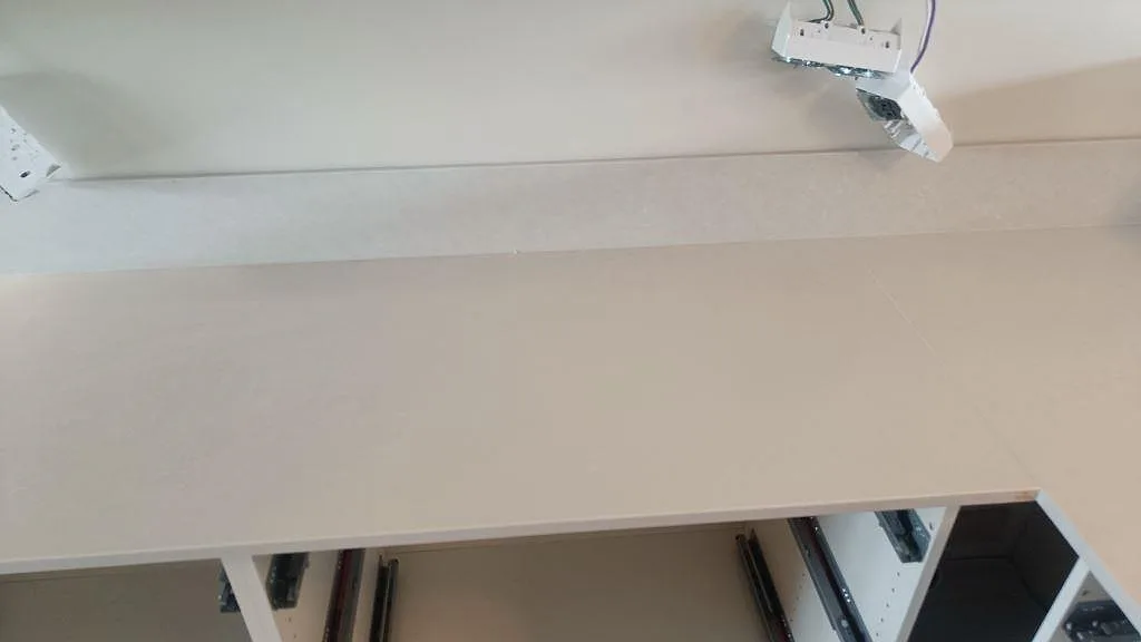 Detalj av ljus Silestone Nolita bänkskiva med 12 mm stänkkant, eldosor och vita köksstommar under montering i Limhamn.