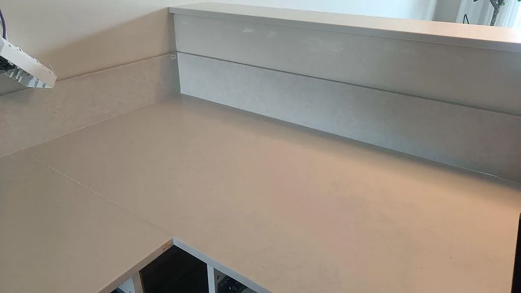Ljus Silestone Nolita bänkskiva i hörn med uppvikt stänkkant och halvö i ett kök under montering i Limhamn.