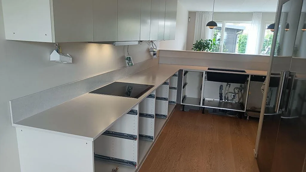 Köksbänkskiva i ljus Silestone Nolita, Mocka, med svart häll, svart underlimmad diskho och låg stänkkant i ett kök i Limhamn.