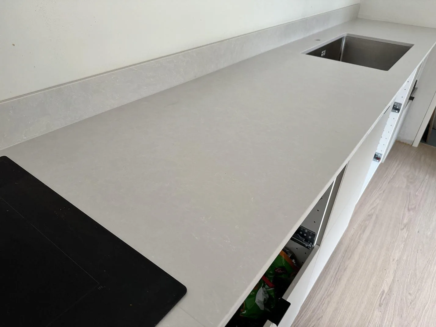 Närbild på köksbänkskiva i Silestone Nolita, matt vit komposit, med stänkskydd och diskhodel i Nättraby.