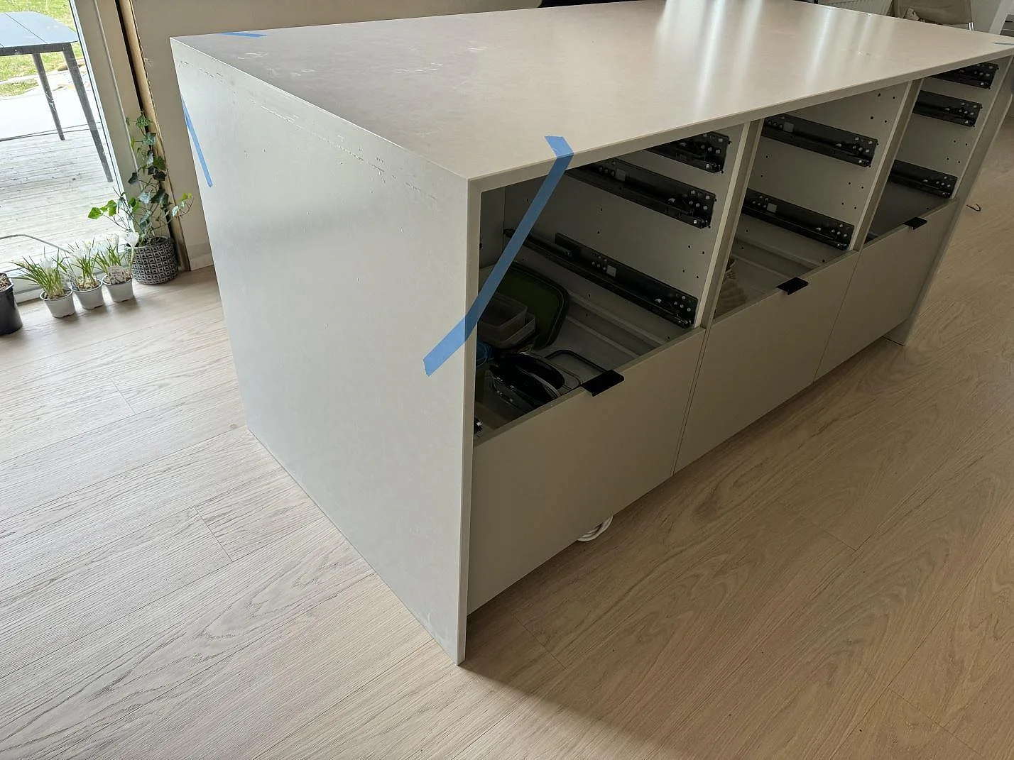 Köksö i vit Silestone Nolita, matt komposit, med tjock neddragen gavel och öppna köksstommar i Nättraby.