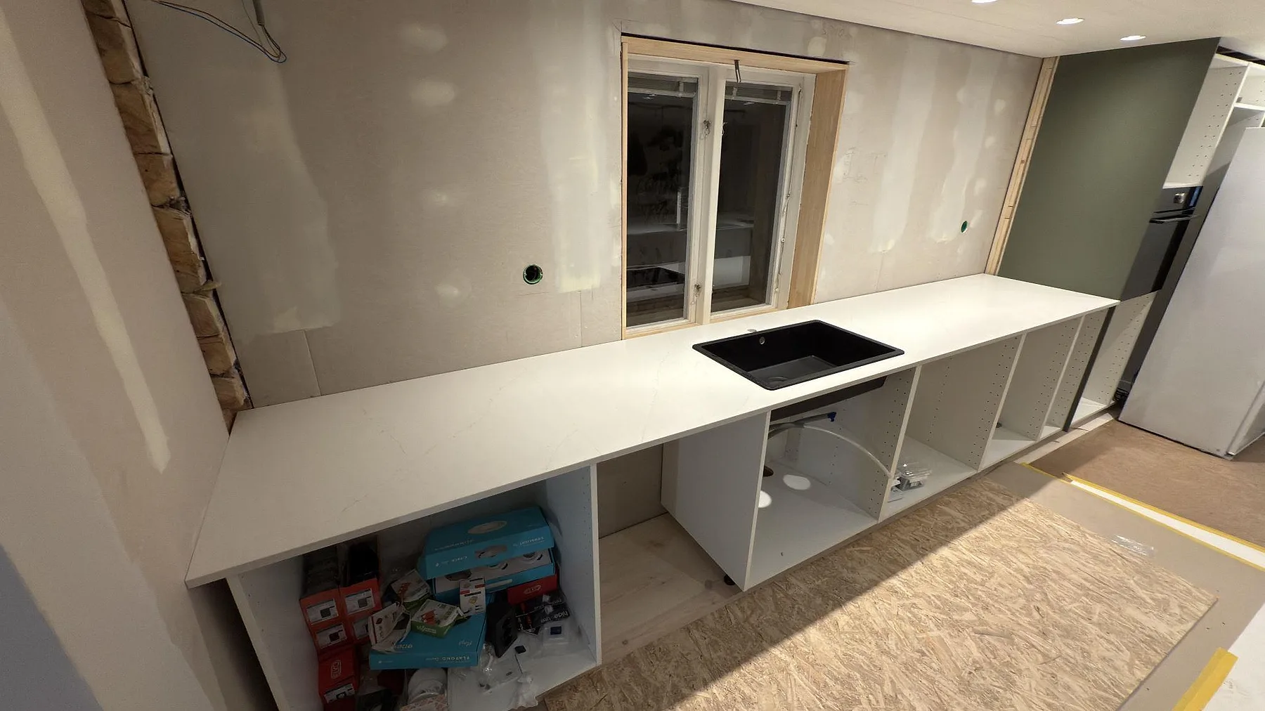 Köksbänkskiva i vit Silestone Persian White, matt 20 mm, med underlimmad svart komposit-diskho längs en fönstervägg i ett kök under montering i Falun.