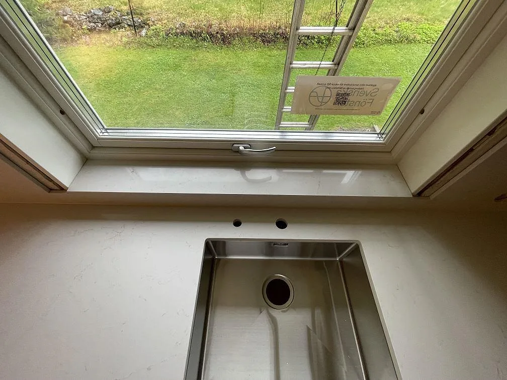 Underlimmad rostfri diskho i polerad Silestone Persian White under ett fönster med trädgårdsutsikt i ett kök i Falun.
