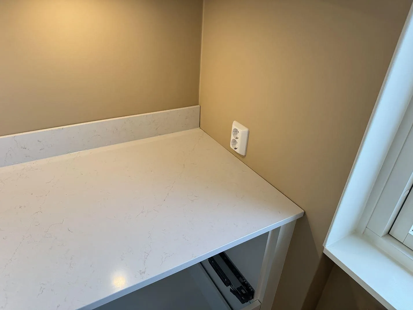 Köksbänkskiva i vit Silestone Persian White i en innerhörna med uppvikt stänkkant i ett kök i Jönköping.