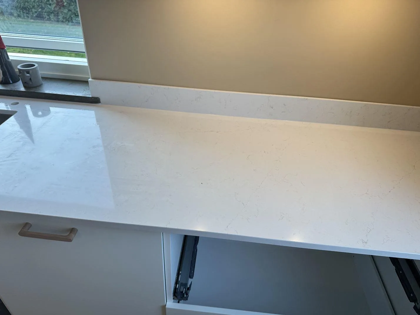 Polerad yta i vit Silestone Persian White med mjuk grå ådring längs köksbänken vid fönstret i ett kök i Jönköping.