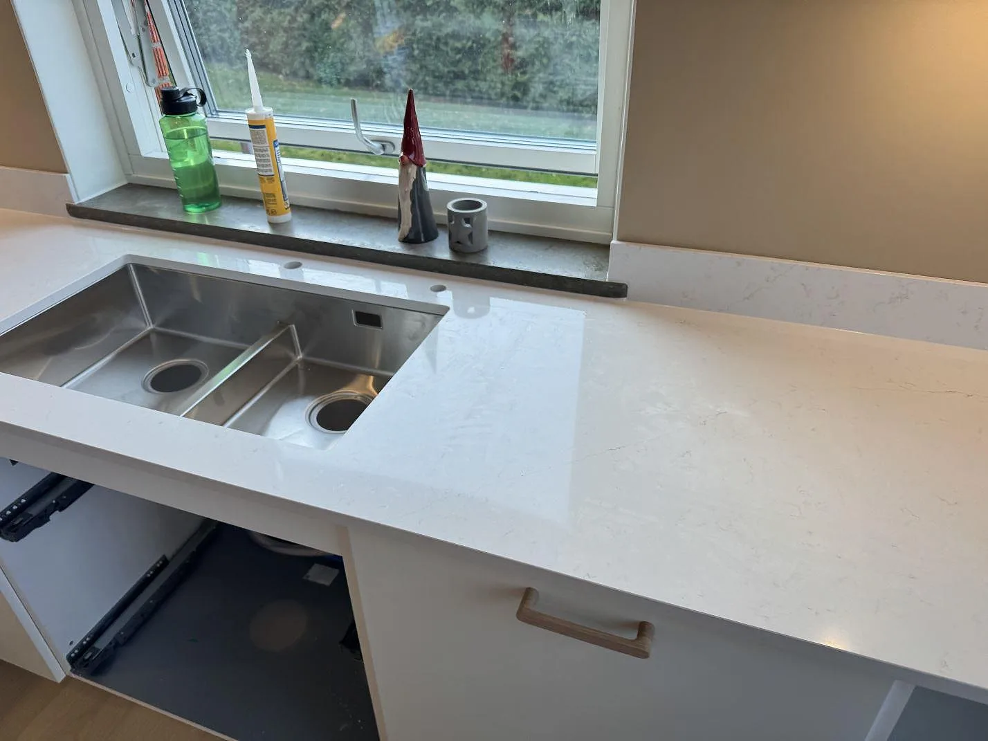 Underlimmad rostfri diskho med dubbla hoar i en polerad köksbänkskiva av vit Silestone Persian White vid fönstret i ett kök i Jönköping.