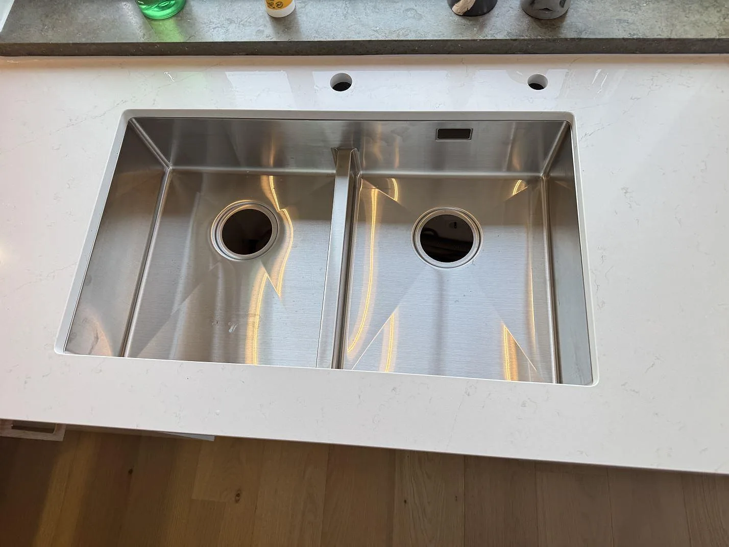 Närbild ovanifrån på den underlimmade rostfria diskhon med dubbla hoar i en köksbänkskiva av vit Silestone Persian White i Jönköping.