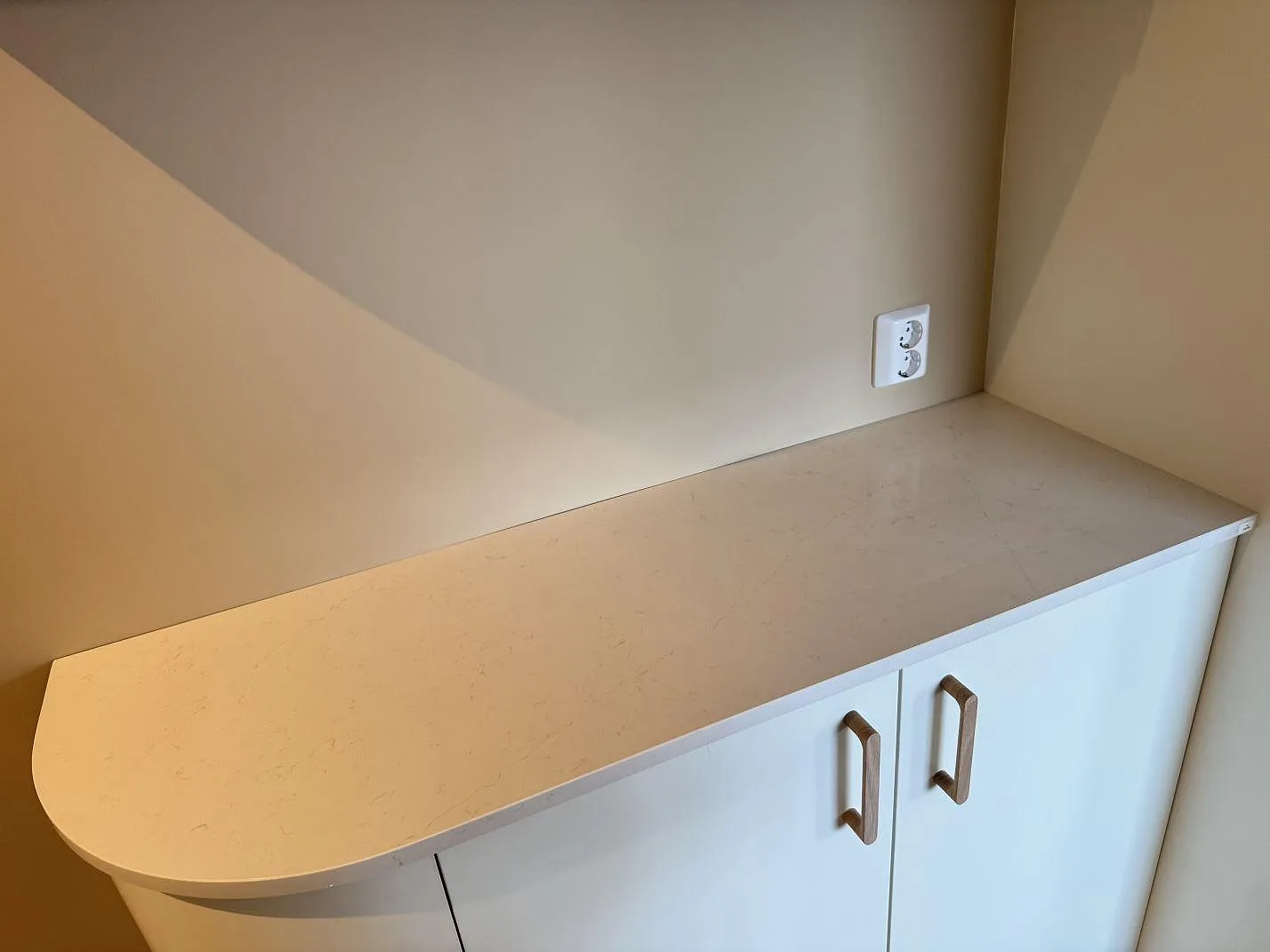 Köksbänkskiva i vit Silestone Persian White, polerad, med en rundad bardiskdel över vita skåp med trähandtag i ett kök i Jönköping.
