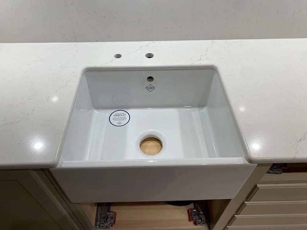 Vit keramisk lågfrontad lantdiskho (farmhouse-modell) underlimmad i polerad Silestone Persian White med borrade blandarhål, i ett kök i Sundbyberg.