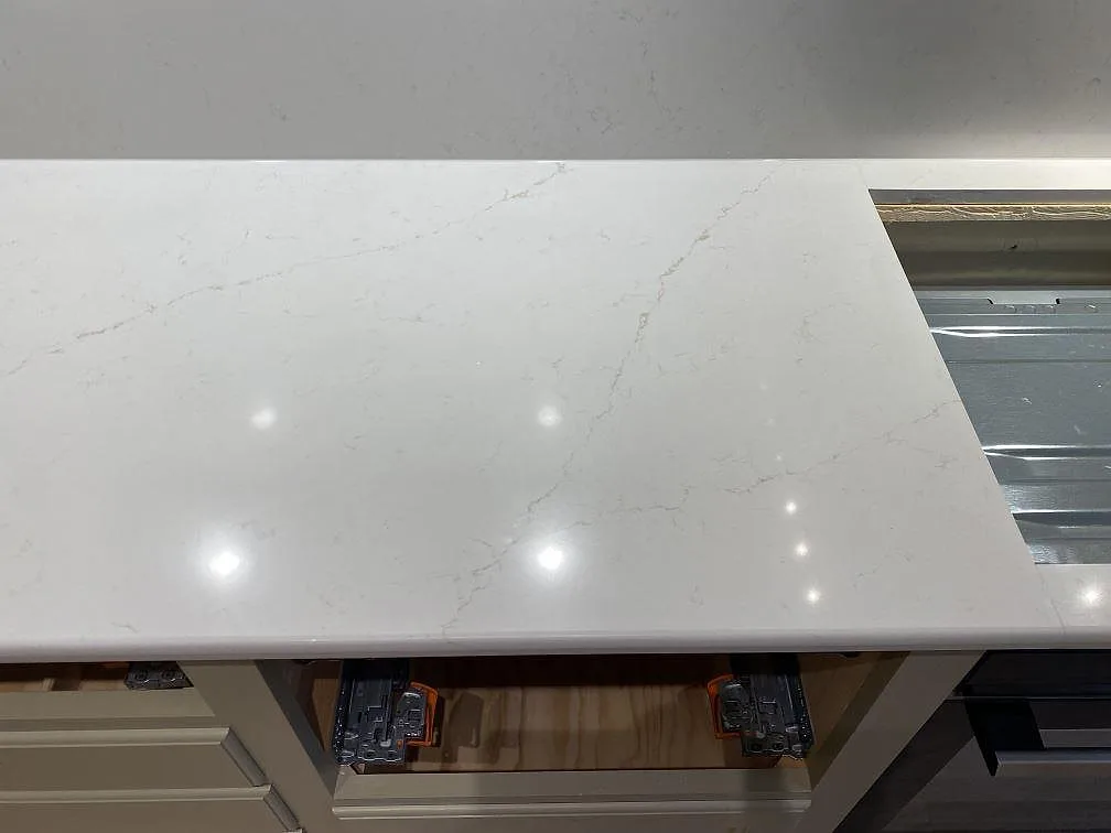 Närbild på den polerade bänkskivan i Silestone Persian White med mjuk grå ådring, monterad ovanpå köksstommarna under montering i Sundbyberg.