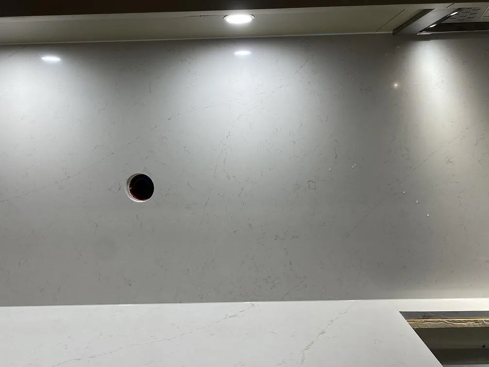 Stänkskydd i samma Silestone Persian White bakom bänken, med urtag för eluttag och spotlights, i ett kök i Sundbyberg.