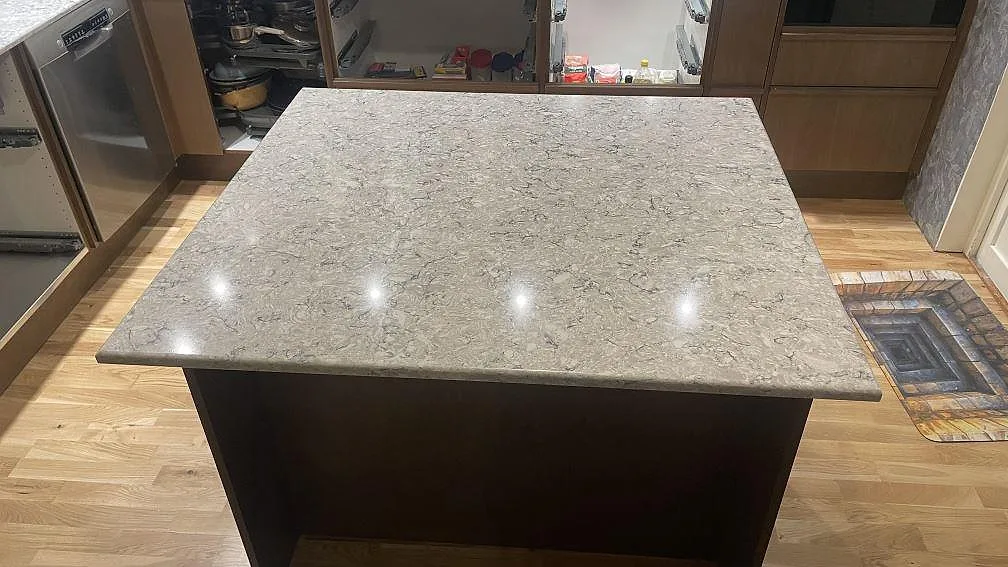 Köksö med blank polerad Silestone Pietra i gråvit kvartskomposit och mörk trästomme i Hällingsjö.