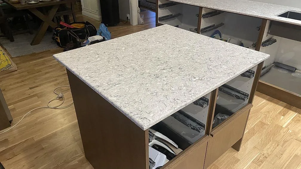 Köksö i polerad Silestone Pietra kvartskomposit med öppen köksstomme och väggbänk i bakgrunden i Hällingsjö.