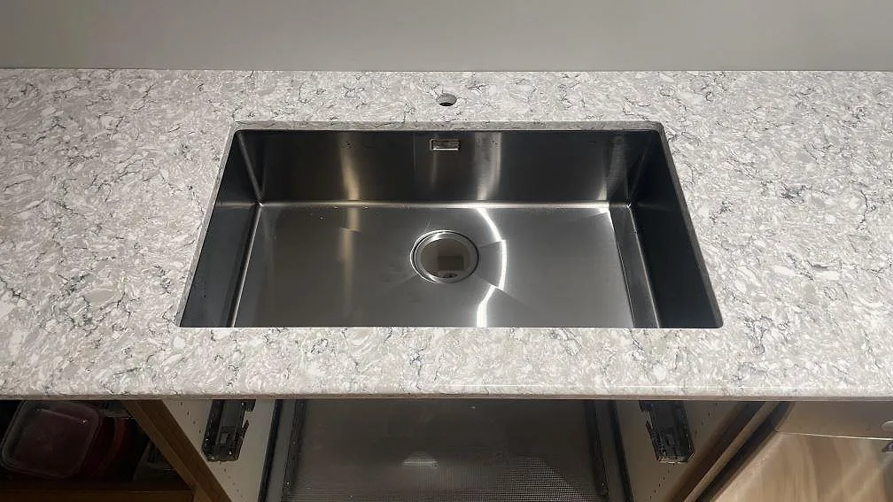 Underlimmad rostfri diskho i polerad Silestone Pietra köksbänkskiva med kranhål bakom hon i Hällingsjö.