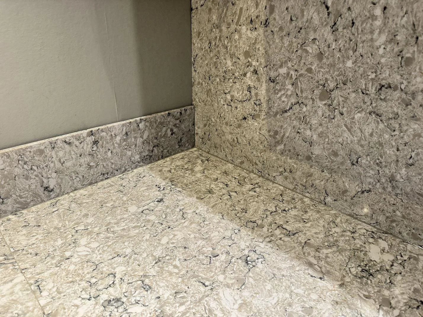 Hörndetalj av polerad Silestone Pietra bänkskiva med uppvikt stänkkant som visar materialets gråvita spräcklighet i Hällingsjö.