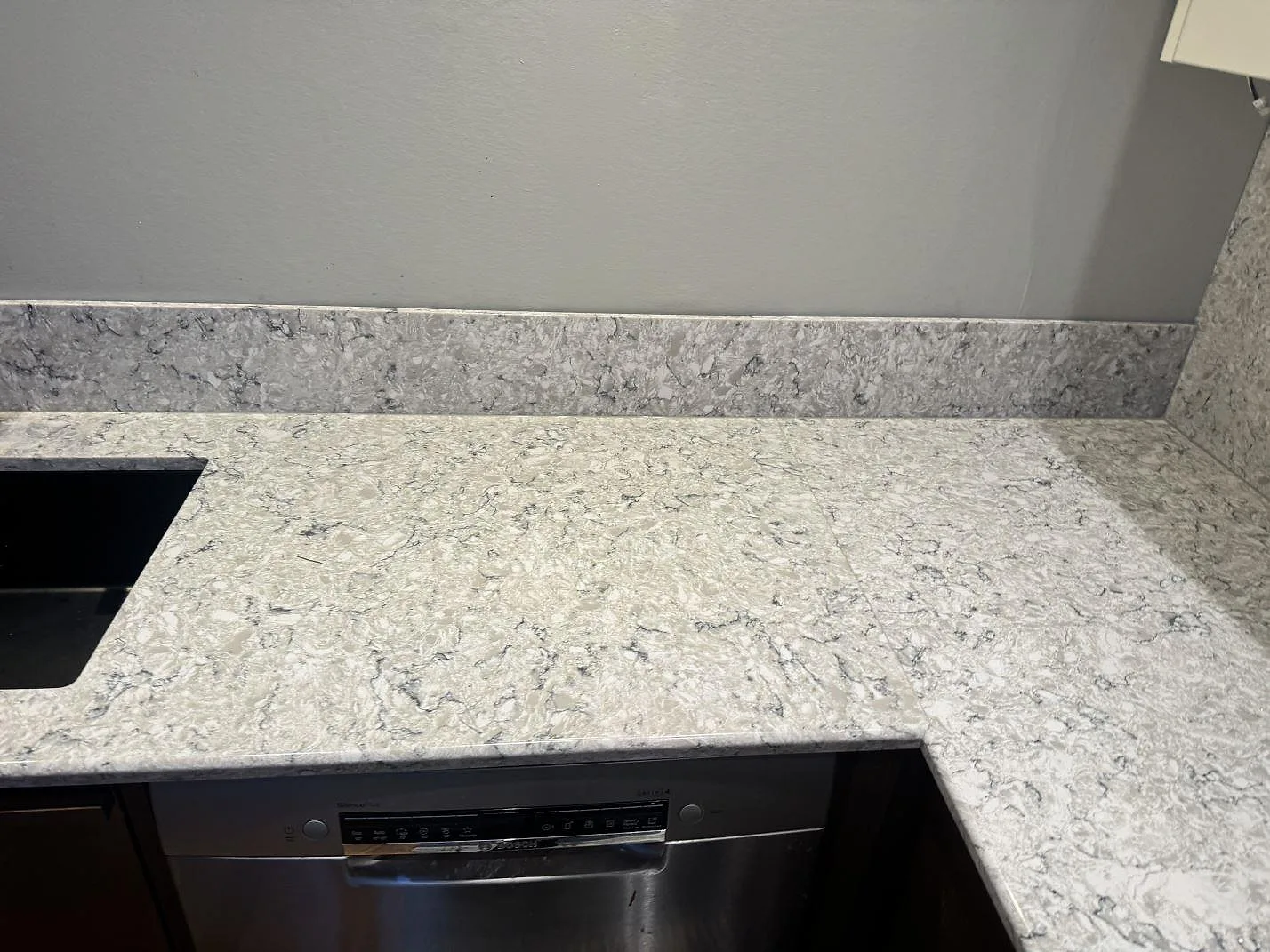 Köksbänkskiva i Silestone Pietra med underlimmad svart diskho och uppvikt stänkkant mot grå vägg i ett kök i Hällingsjö.