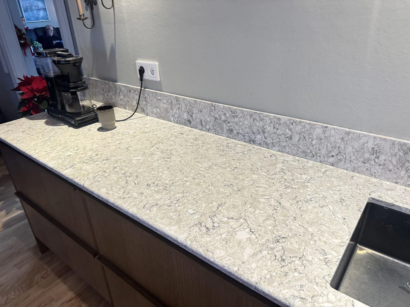 Köksö i Silestone Pietra med polerad yta och livfull gråvit spräcklighet, monterad över mörka träluckor i ett kök i Hällingsjö.