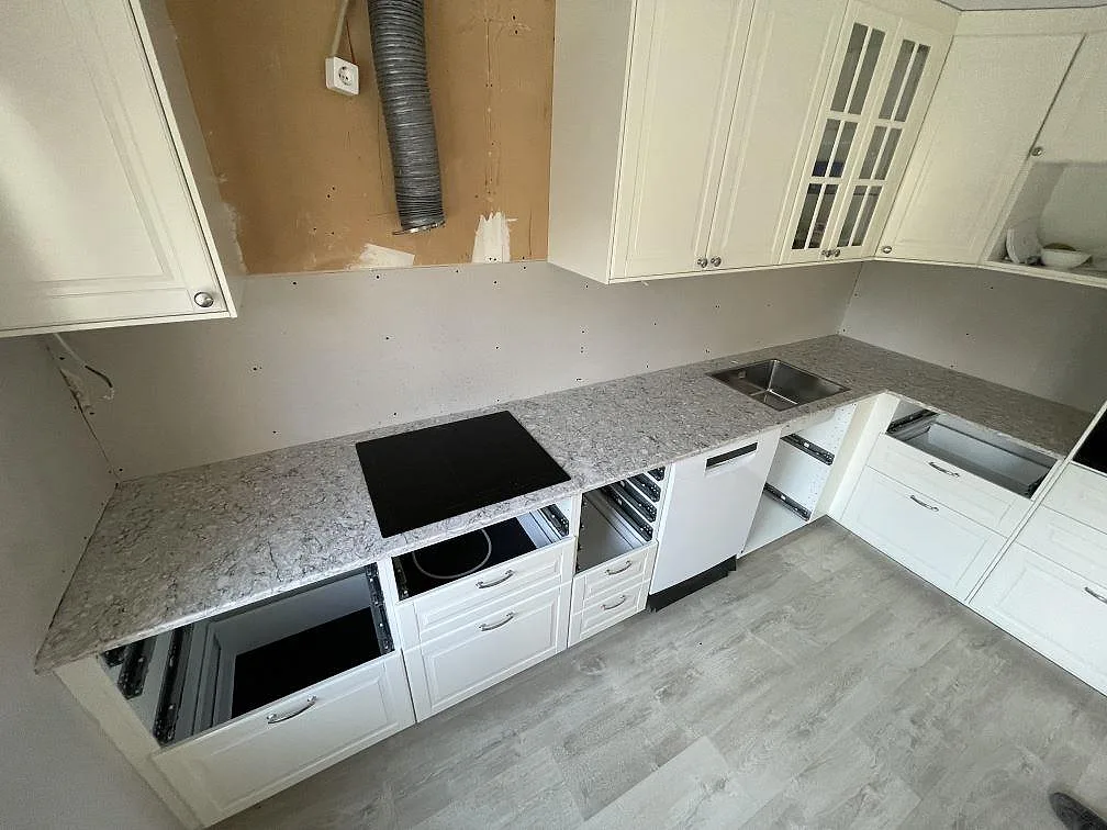 Köksbänkskiva i grå Silestone Pietra, polerad, monterad som L-formad bänk i ett kök under montering i Järfälla, med underlimmad rostfri diskho och infälld induktionshäll.