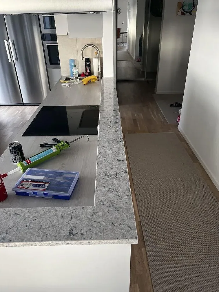 Närbild av köksöns polerade Silestone Pietra bänkskiva i komposit med svart induktionshäll och ljusa stommar i Malmö.