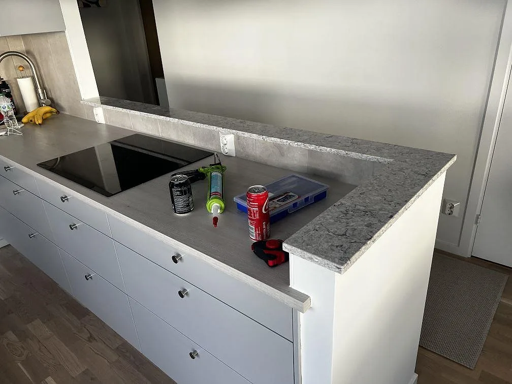 L-formad bänkskiva i polerad Silestone Pietra med stänkkant och svart induktionshäll under montering i Malmö.