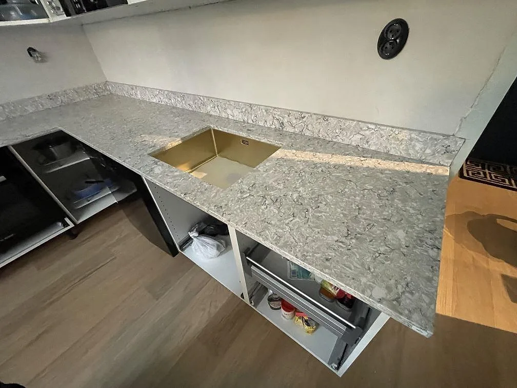 Närbild på mässingsfärgad underlimmad diskho i en polerad bänkskiva av Silestone Pietra i ett kök i Stockholm.