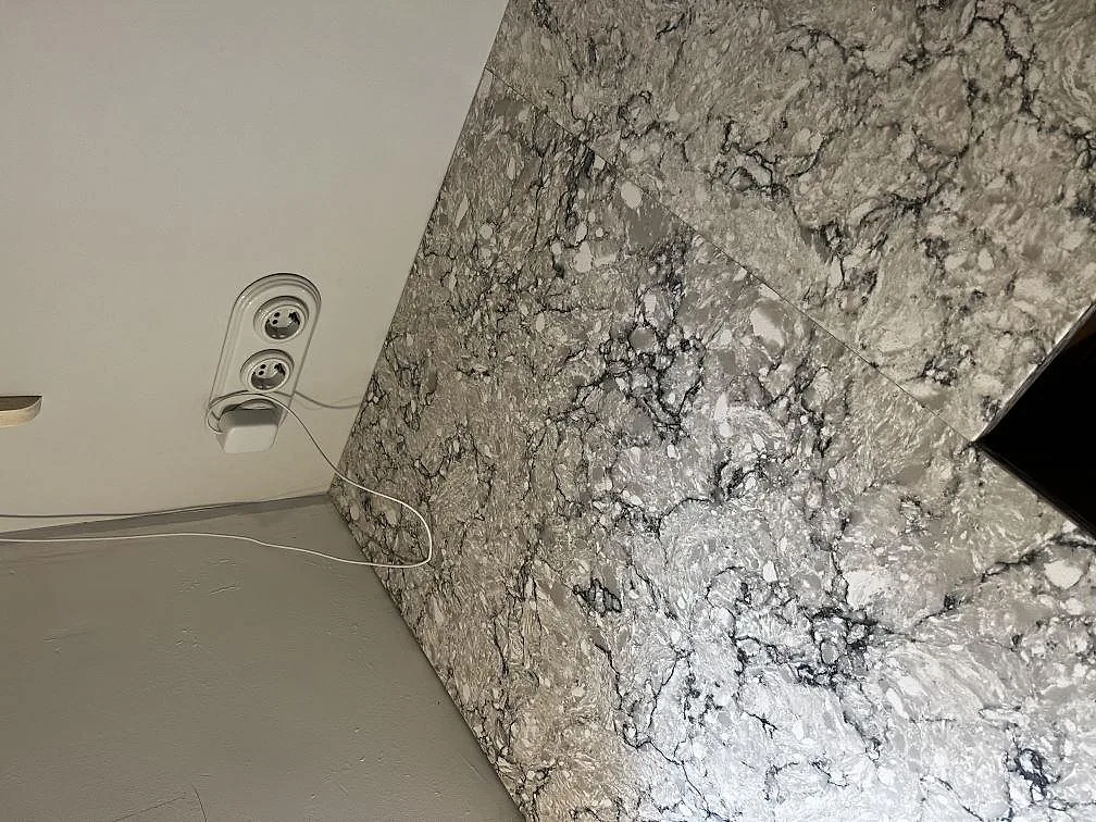 Närbild på bänkskiva och stänkkant i polerad Silestone Pietra med grå teckning och vägguttag i Tygelsjö.