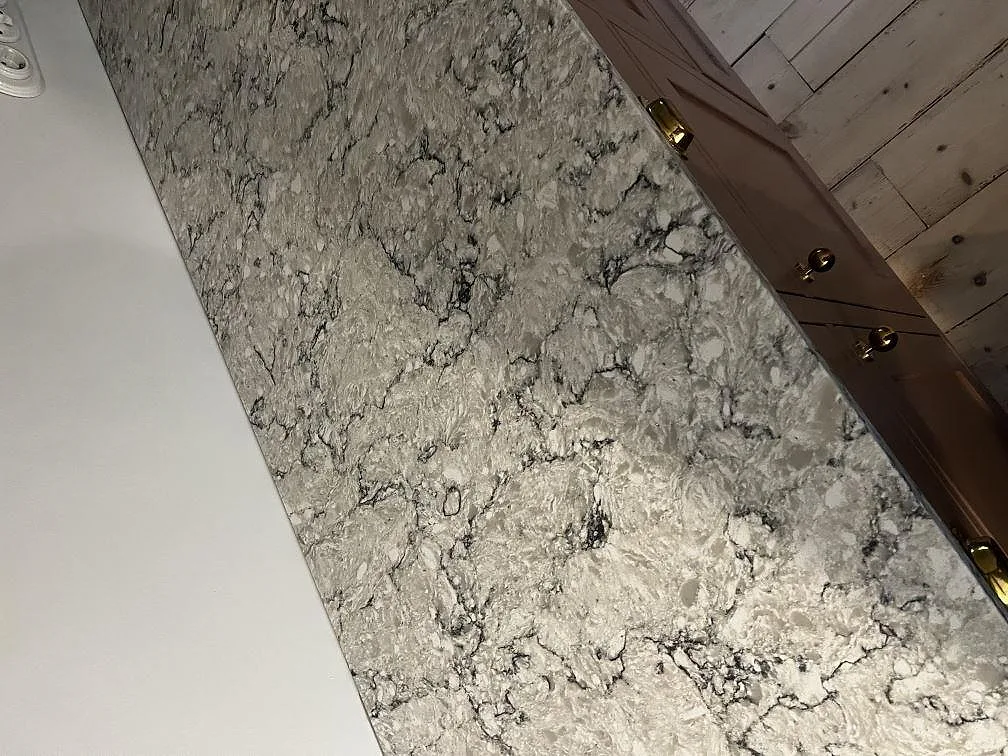 Lång bänkyta i polerad Silestone Pietra med grå stenstruktur mot träinredning och trägolv i Tygelsjö.