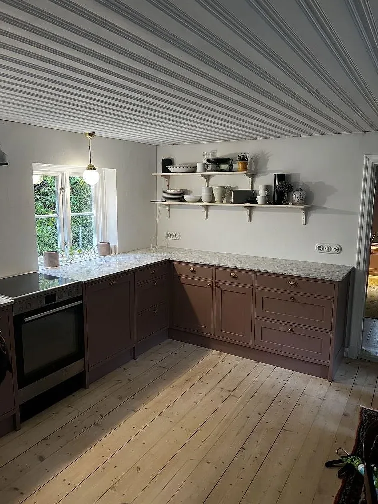 Översiktsbild av kök i Tygelsjö med bänkskiva och låg stänkkant i polerad Silestone Pietra ovanpå träinredning.