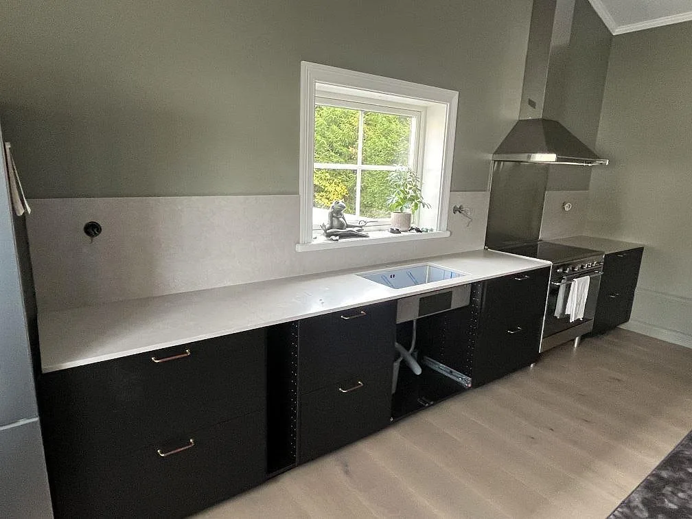 Lång köksbänkskiva i matt Silestone Poblenou Mocka, ljus kvartskomposit, med underlimmad rostfri diskho i ett kök med svarta skåp i Leksand.