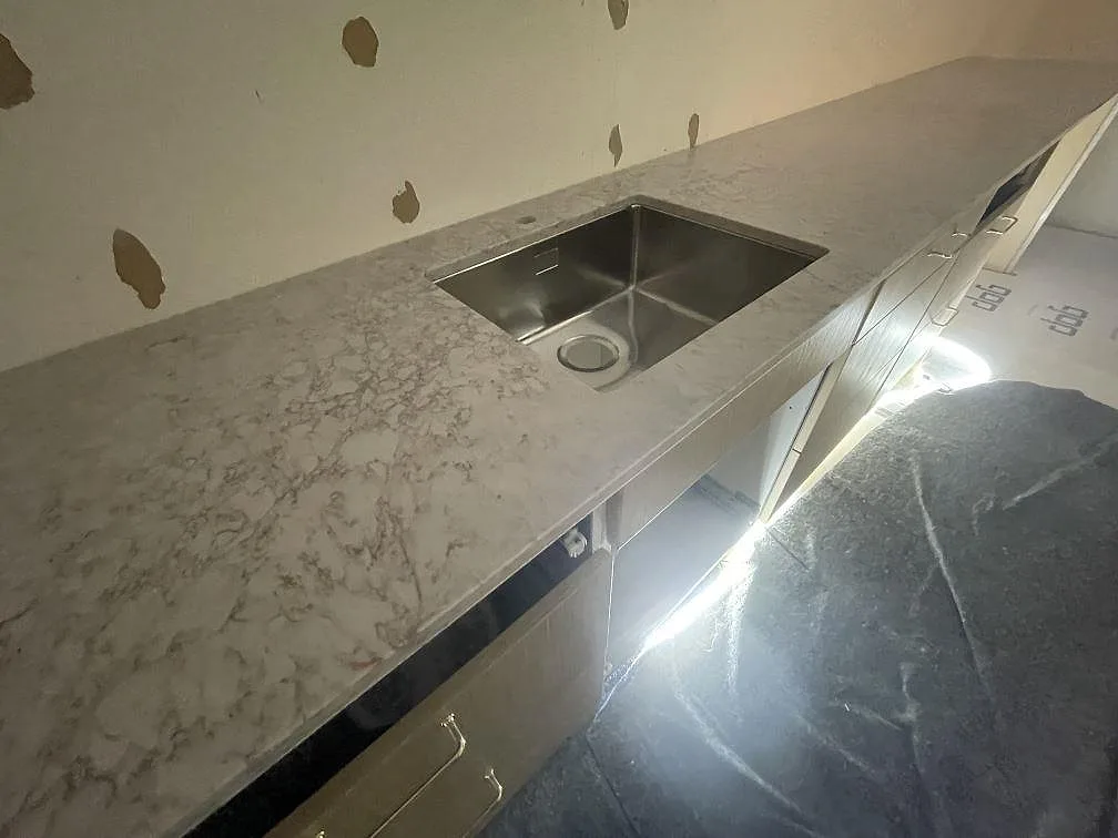 Underlimmad rostfri diskho i köksbänkskiva av Silestone Riviere Rose, ljus kvartskomposit med mjuk grå ådring, i ett kök i Vaxholm.