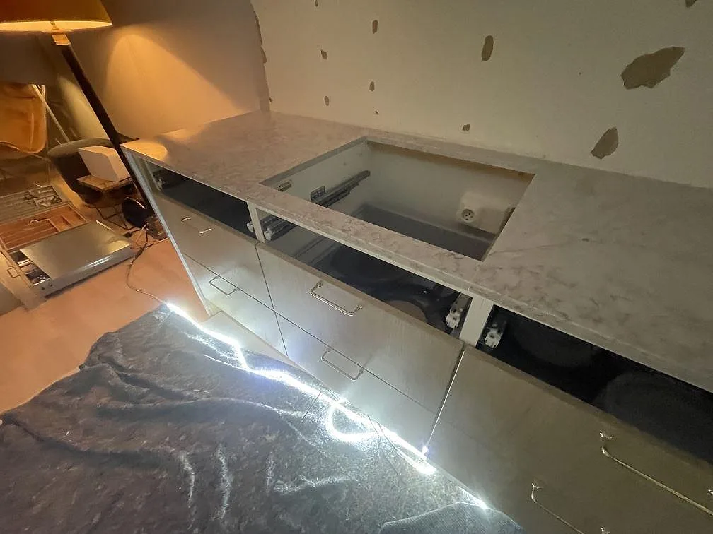 Köksbänkskiva i Silestone Riviere Rose med urtag för häll över öppna lådstommar, ljus kvartskomposit i ett kök under montering i Vaxholm.