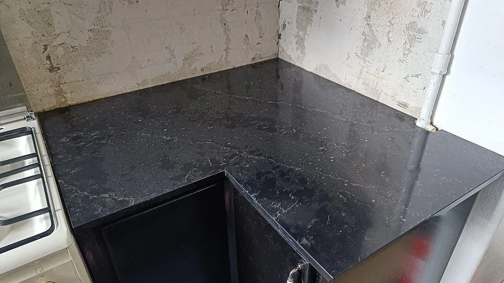 Köksbänkskiva i mörk Silestone Romantic Ash, polerad komposit, monterad i vinkel vid fristående spis i Malmö.