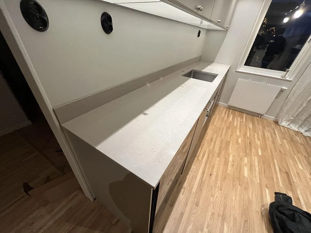 Väggbänk i ljus Silestone Royal Reef, polerad kompositsten med uppvikt stänkskydd och fönster i ett kök i Bålsta.