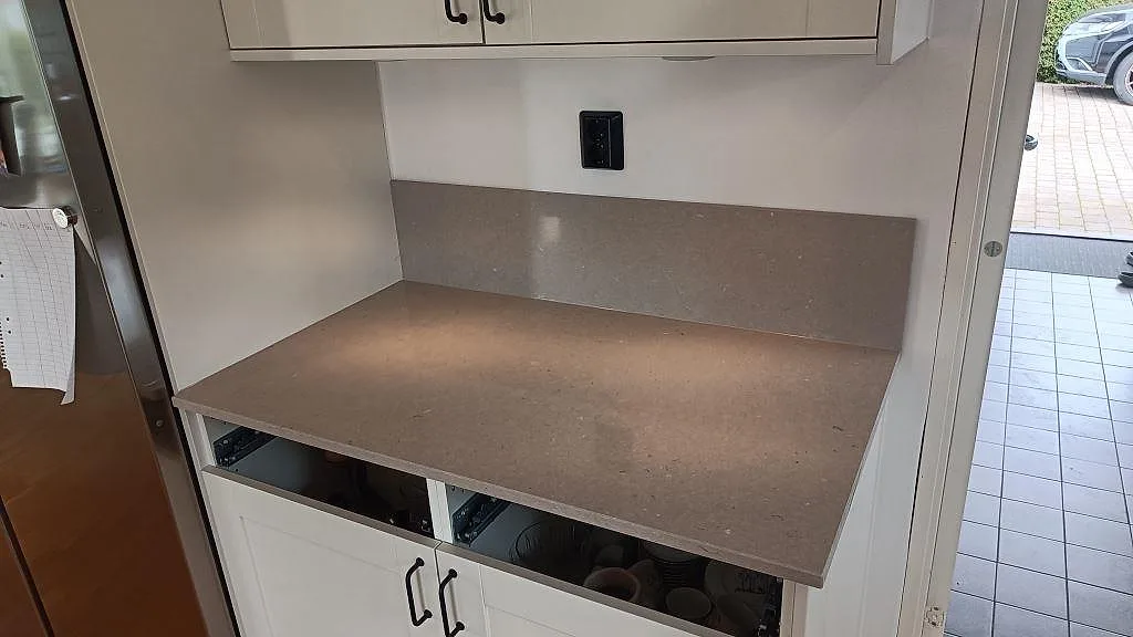 Sidobänk i polerad Silestone Royal Reef med matchande stänkskydd, monterad mellan högskåp och dörröppning i Barsebäck.