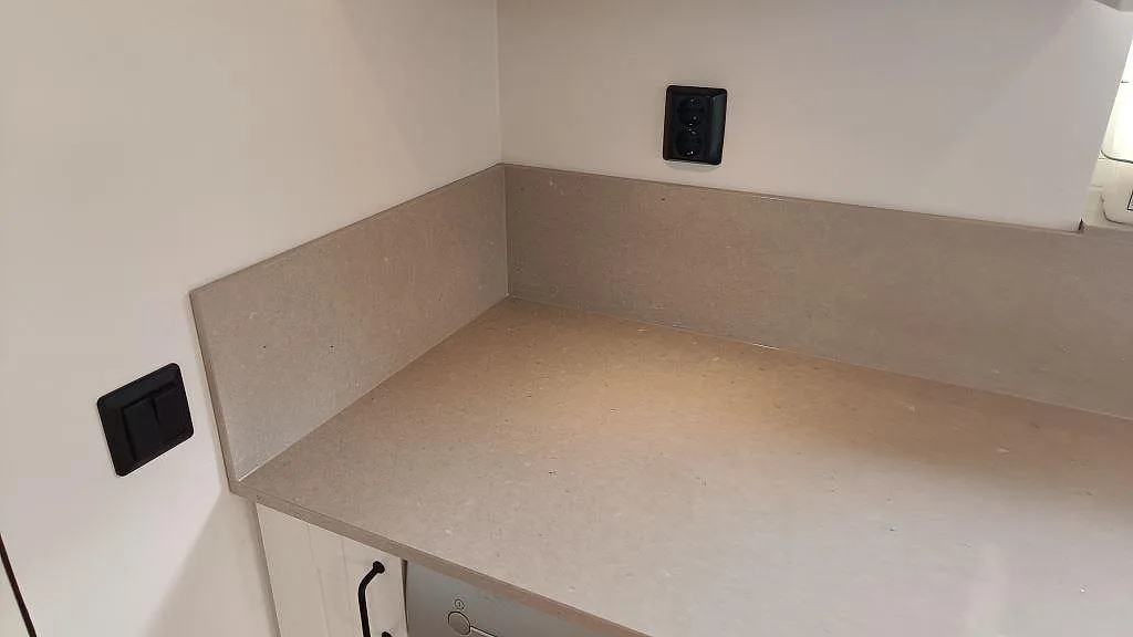 Hörndetalj av polerad Silestone Royal Reef, kvartskomposit, med låg stänkkant och svarta eluttag i köket i Barsebäck.