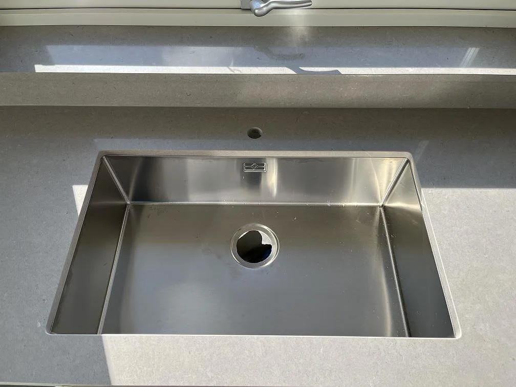 Underlimmad rostfri diskho i polerad Silestone Royal Reef med låg stänkkant och solljus i Bergkvara.