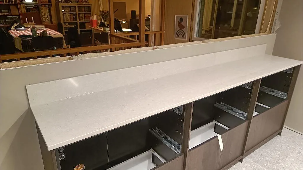 Lång bänkskiva med uppvikt stänkkant i Silestone Royal Reef, ljus kvartskomposit med blandad Mocka och Polerad finish, i Bjärred.
