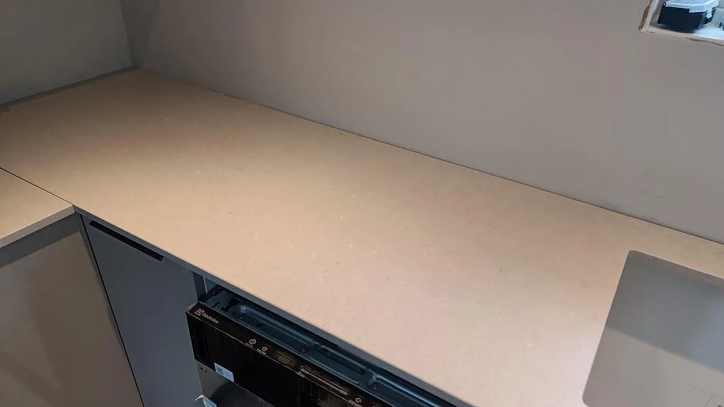 Rak köksbänkskiva i matt beige Silestone Royal Reef ovanför ett diskmaskinsutrymme i ett kök i Fagerfjäll.