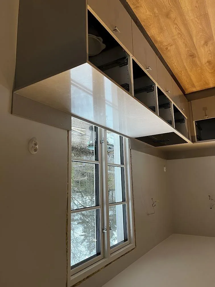 Köksbänkskiva i vit Silestone Royal Reef, polerad, i L-format längs en fönstervägg med öppna stommar under montering i ett kök i Göteborg.