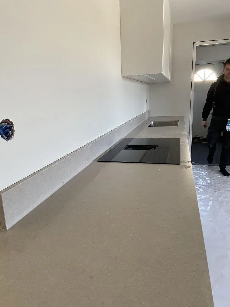 Bänkskiva i matt Silestone Royal Reef med uppvikt kant mot vägg i ett kök under montering i Hässleholm.
