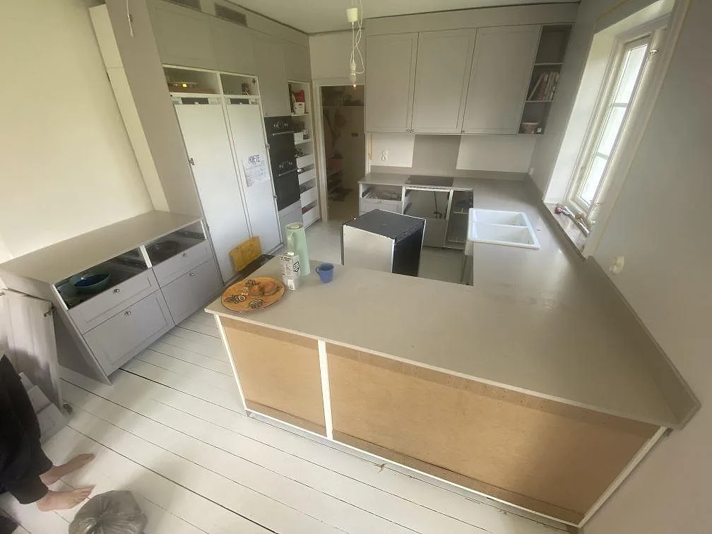 U-format kök i Helsingborg med köksbänkskivor och en bred halvö i Silestone Royal Reef, en matt gråbeige kvartskomposit, med vit keramikho och svart induktionshäll under montering.