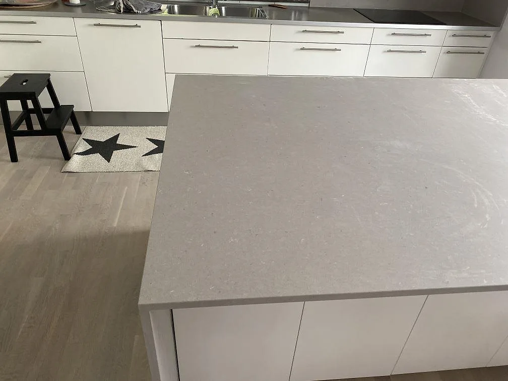Köksö i matt Silestone Royal Reef med ljus komposityta, vita köksluckor och svart induktionshäll i Höllviken.