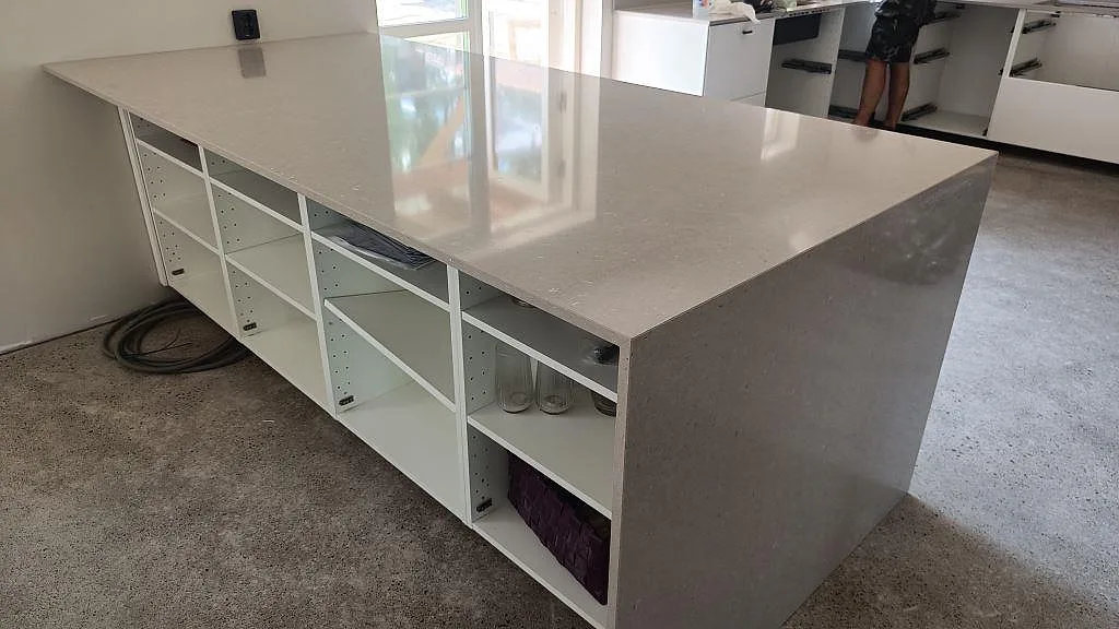 Stor köksö i greige Silestone Royal Reef, polerad kvartskomposit, med öppen hyllbas och neddragen sida i ett kök i Höllviken.